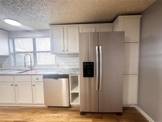 kitchen featuring white cabinets, a sink, light wood-style floors, stainless steel appliances, and decorative backsplash