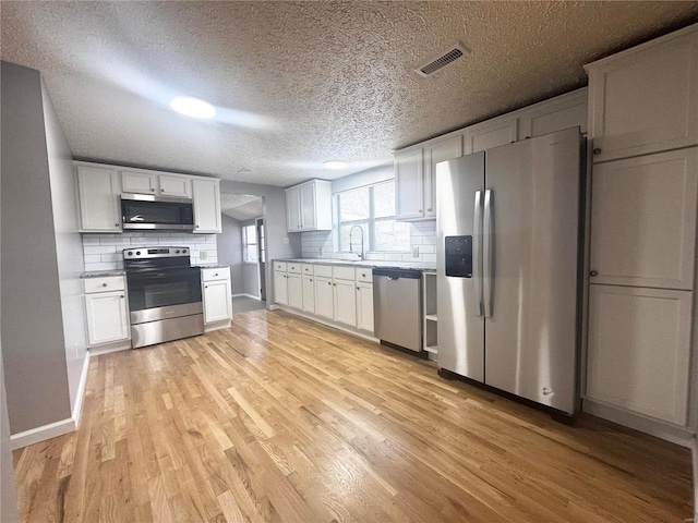 kitchen with light wood finished floors, backsplash, and stainless steel appliances