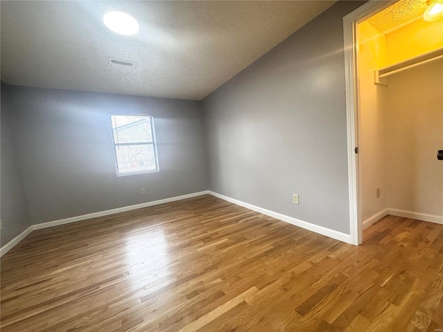 interior space featuring baseboards, a textured ceiling, visible vents, and wood finished floors