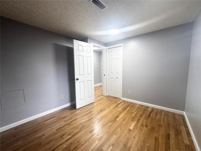 unfurnished bedroom featuring baseboards, a textured ceiling, wood finished floors, and visible vents