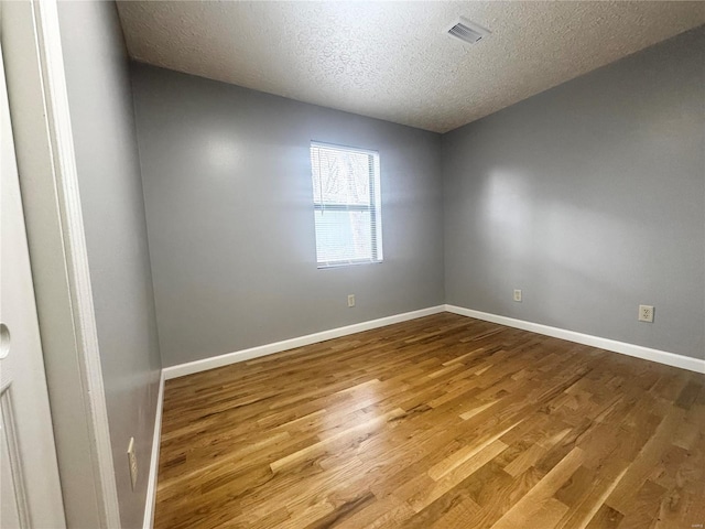 spare room with baseboards, a textured ceiling, visible vents, and wood finished floors