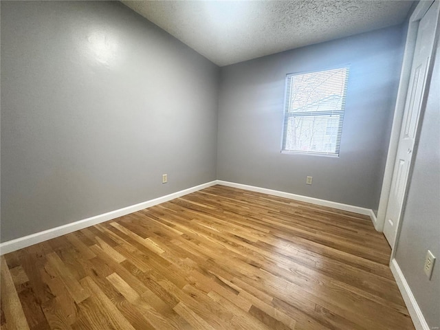 empty room with baseboards, a textured ceiling, and wood finished floors