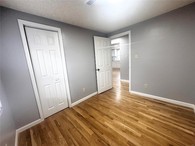 unfurnished bedroom with a textured ceiling, baseboards, visible vents, and light wood finished floors