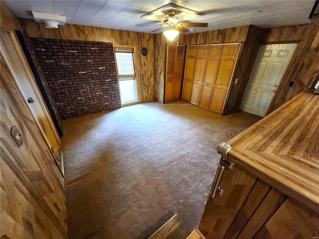 unfurnished bedroom featuring a closet, light carpet, a ceiling fan, and wood walls