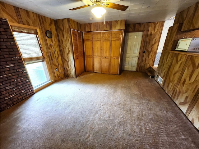 unfurnished bedroom with light colored carpet, ceiling fan, wood walls, and visible vents