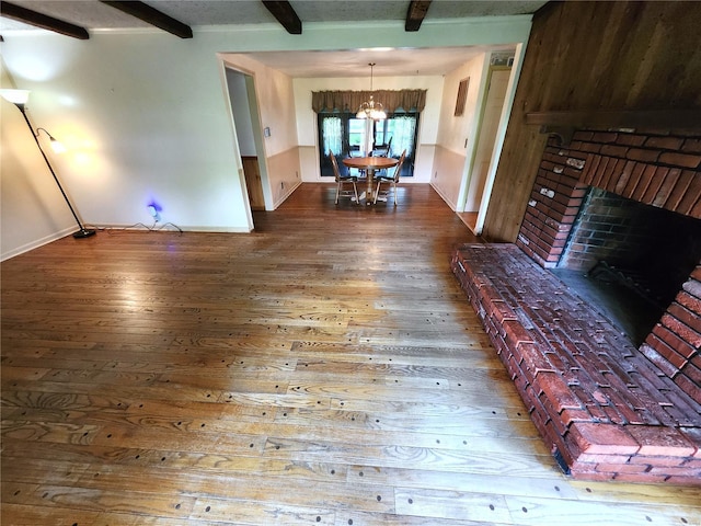 living area featuring wood-type flooring, an inviting chandelier, beam ceiling, a fireplace, and baseboards