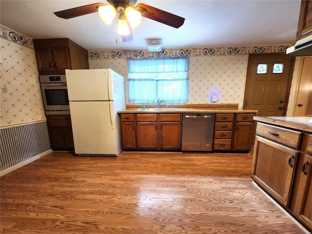 kitchen featuring a sink, light wood-style flooring, stainless steel appliances, wallpapered walls, and a ceiling fan