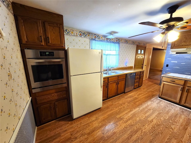 kitchen featuring wallpapered walls, a sink, light wood finished floors, appliances with stainless steel finishes, and exhaust hood