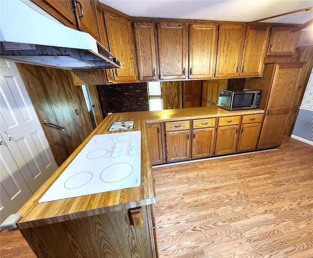 kitchen with brown cabinetry, white electric cooktop, light wood-type flooring, stainless steel microwave, and under cabinet range hood