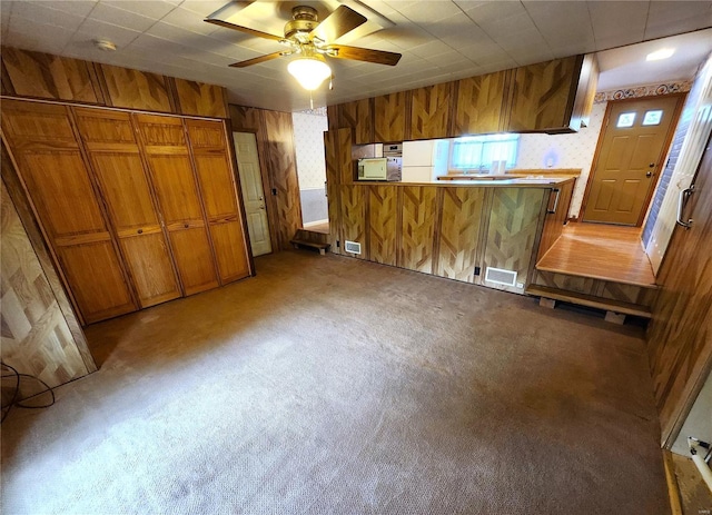 interior space with wooden walls, light carpet, brown cabinets, and visible vents