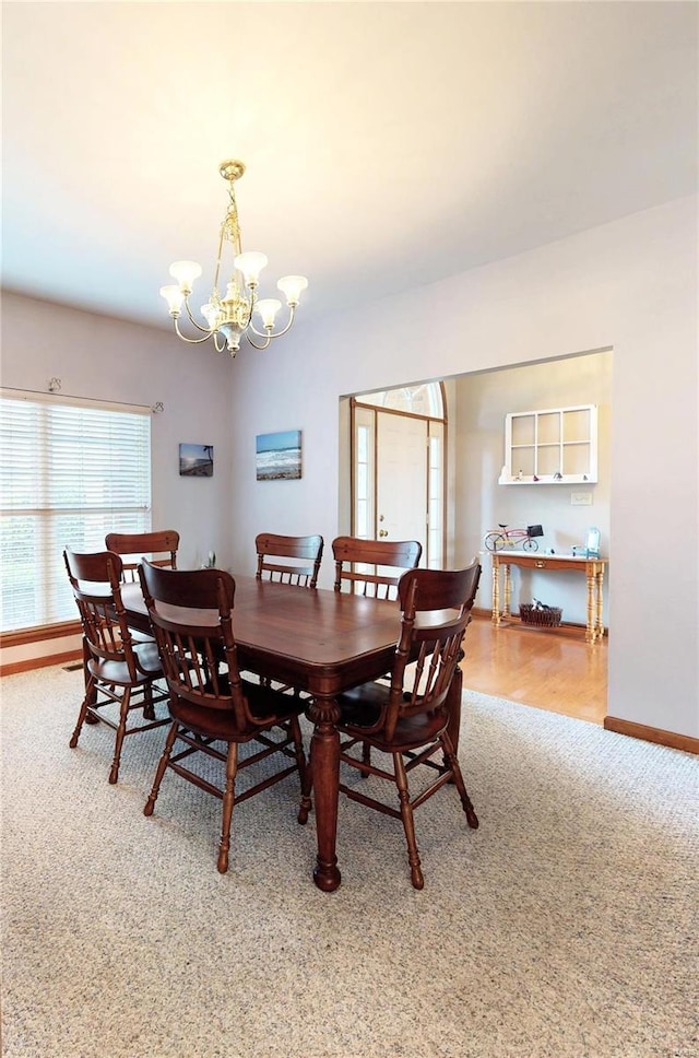 dining space with baseboards, a notable chandelier, and light carpet