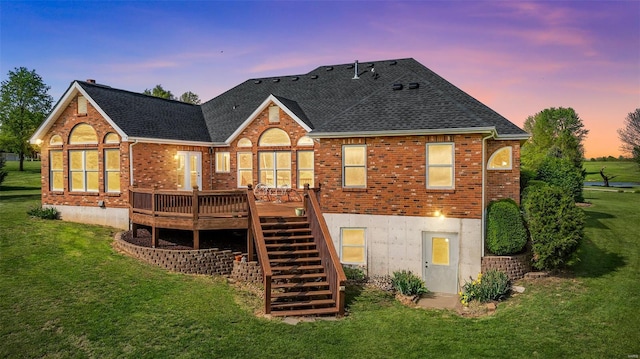 back of property at dusk featuring stairway, brick siding, a lawn, and a deck