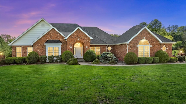 view of front of property featuring a shingled roof, a front yard, and brick siding