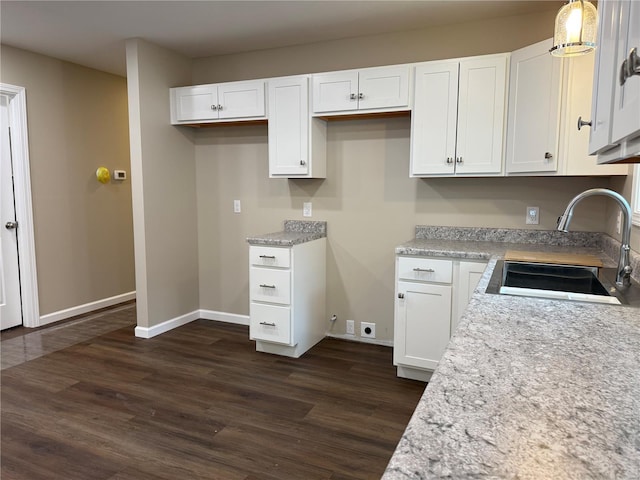 kitchen featuring dark wood-style flooring, baseboards, white cabinetry, a sink, and hanging light fixtures