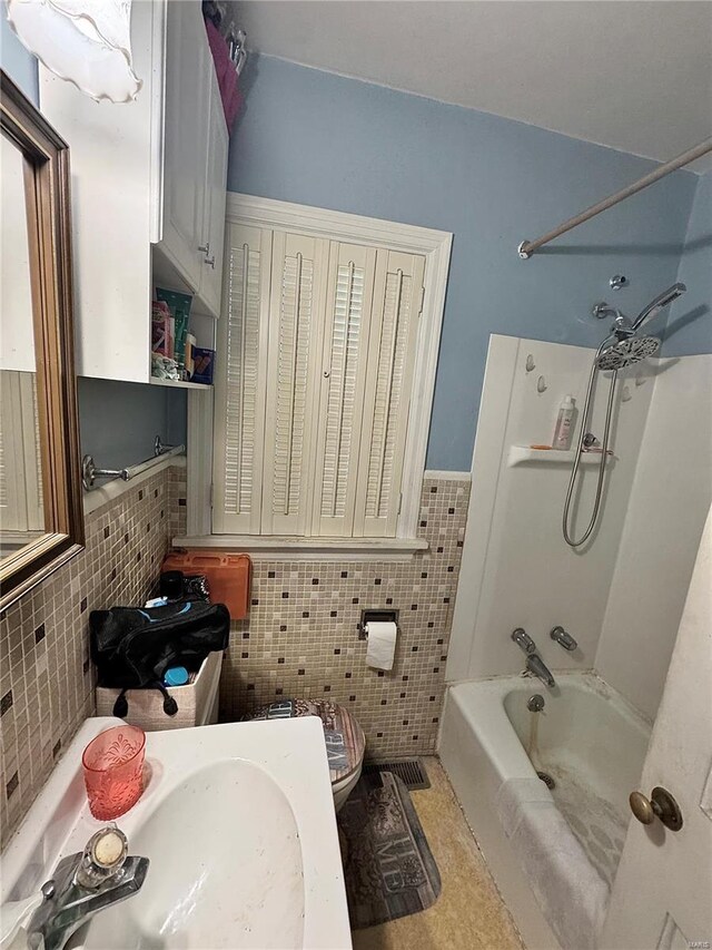 bathroom with tile walls, a sink, a wainscoted wall, toilet, and bathing tub / shower combination