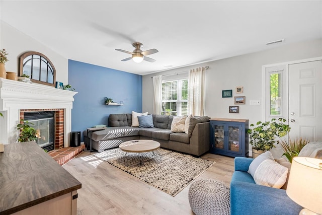 living area with a fireplace, a ceiling fan, wood finished floors, and visible vents