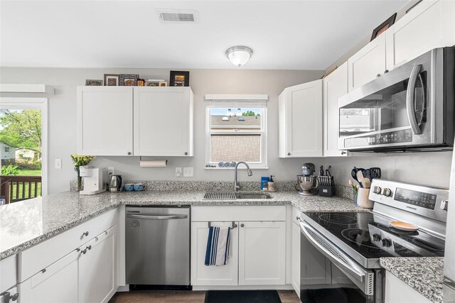 kitchen with visible vents, light stone countertops, white cabinets, a sink, and appliances with stainless steel finishes