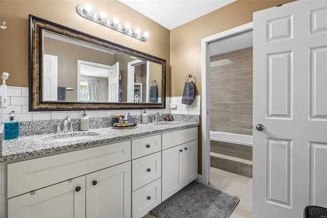 full bath featuring double vanity, a sink, tile patterned flooring, and a relaxing tiled tub