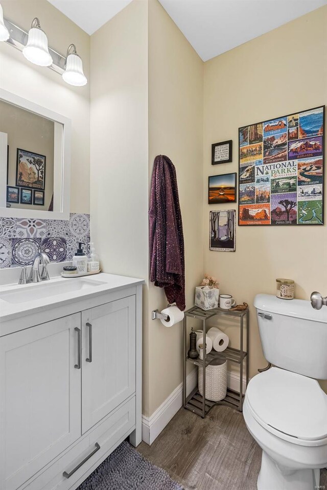 half bathroom featuring baseboards, vanity, toilet, and wood finished floors
