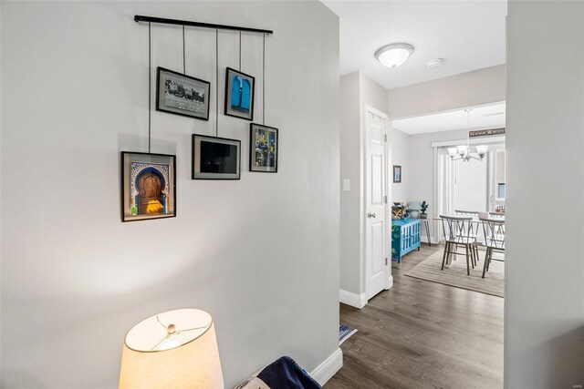 hallway with baseboards, wood finished floors, and a notable chandelier