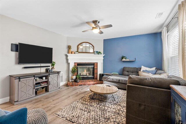 living room with visible vents, a brick fireplace, baseboards, ceiling fan, and light wood finished floors