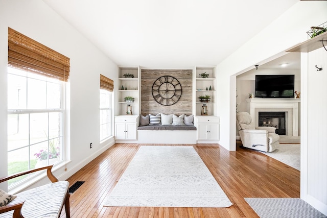 unfurnished living room featuring baseboards, a glass covered fireplace, built in features, and light wood finished floors