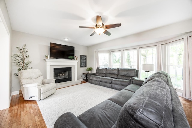 living room with a glass covered fireplace, baseboards, a ceiling fan, and wood finished floors