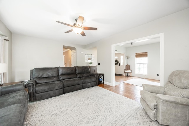 living room with baseboards, arched walkways, ceiling fan, and wood finished floors