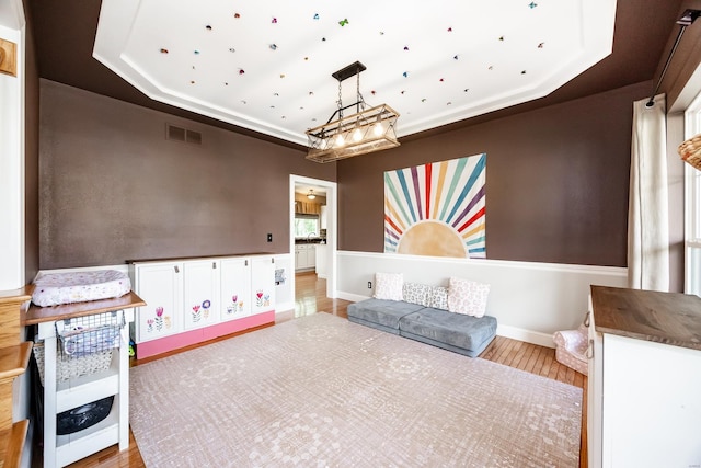 game room with an inviting chandelier, baseboards, wood finished floors, a tray ceiling, and visible vents