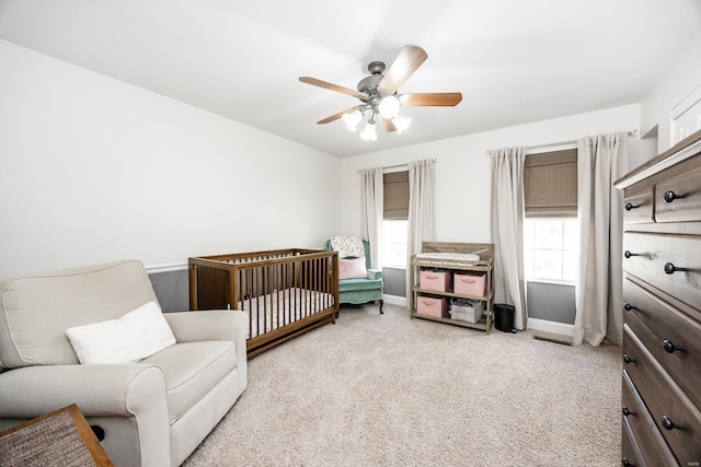 bedroom featuring a crib, baseboards, carpet, and a ceiling fan