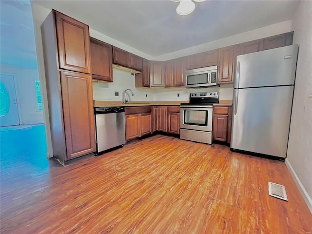 kitchen with appliances with stainless steel finishes, a sink, light wood finished floors, light countertops, and visible vents