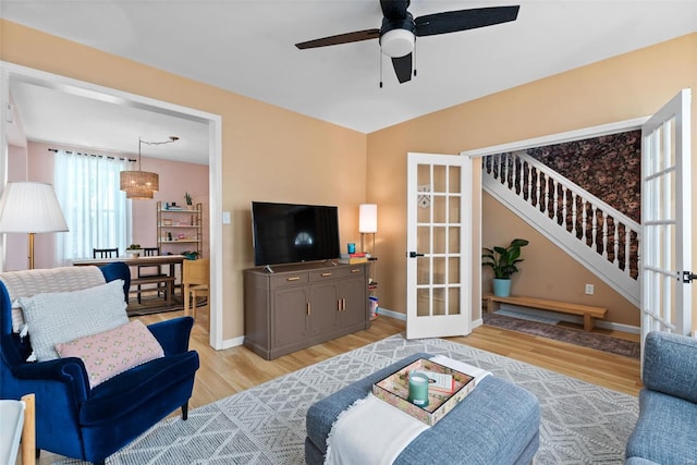 living area featuring ceiling fan, french doors, stairway, baseboards, and light wood-style floors