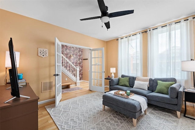 living room featuring visible vents, stairs, light wood-type flooring, french doors, and a ceiling fan