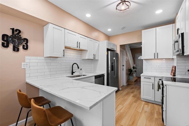kitchen with light stone countertops, a sink, a breakfast bar area, stainless steel appliances, and a peninsula
