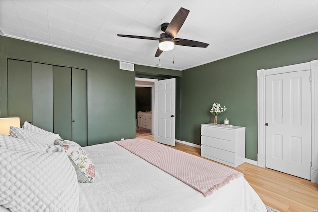 bedroom with visible vents, a closet, wood finished floors, baseboards, and ceiling fan