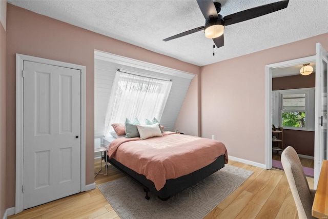 bedroom with baseboards, a ceiling fan, a textured ceiling, and light wood-style flooring