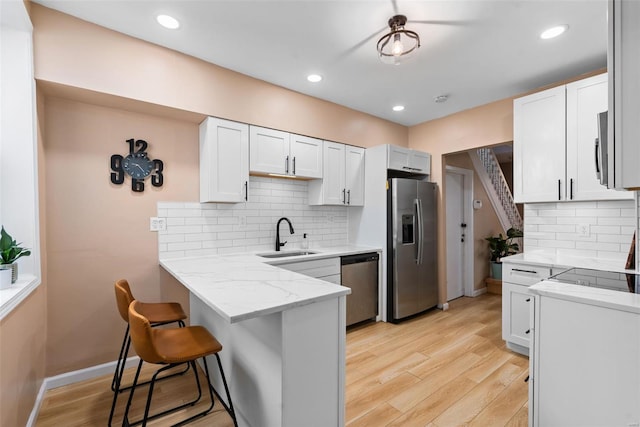 kitchen with a sink, appliances with stainless steel finishes, a kitchen bar, and light wood-style flooring