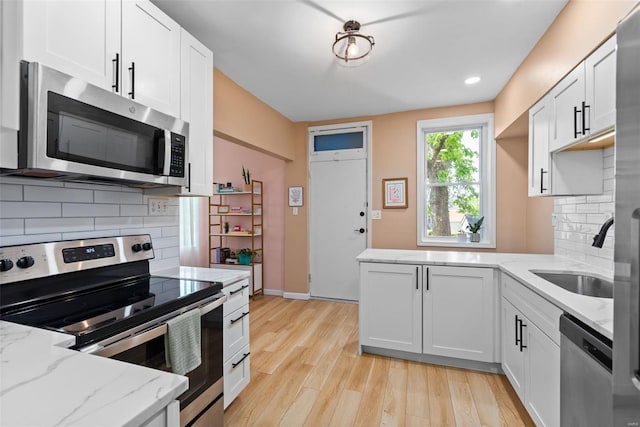 kitchen with appliances with stainless steel finishes, decorative backsplash, a sink, and light wood-style flooring