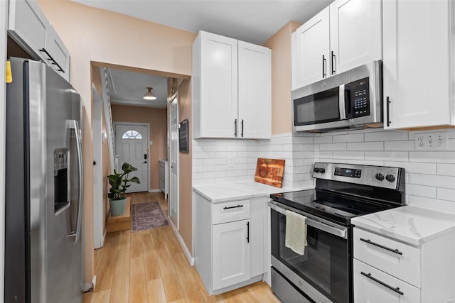 kitchen with light stone countertops, light wood-type flooring, white cabinetry, tasteful backsplash, and stainless steel appliances