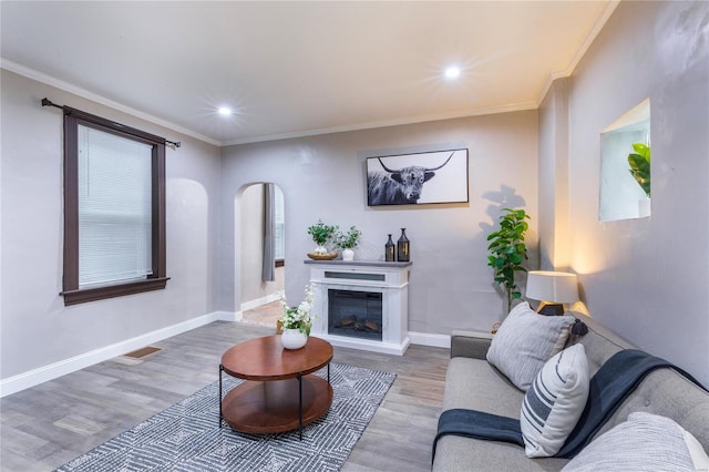 living area with arched walkways, visible vents, ornamental molding, and wood finished floors