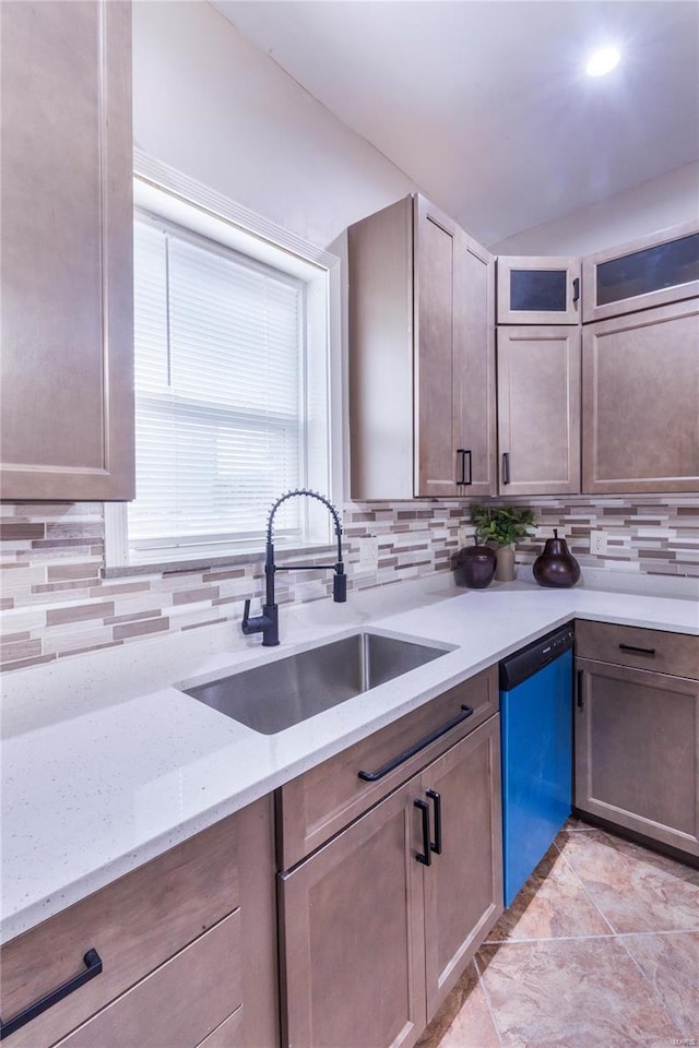 kitchen featuring light stone counters, a sink, dishwashing machine, and tasteful backsplash