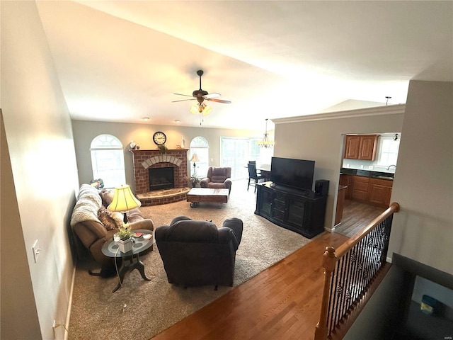 living area featuring ceiling fan, a fireplace, vaulted ceiling, wood finished floors, and baseboards