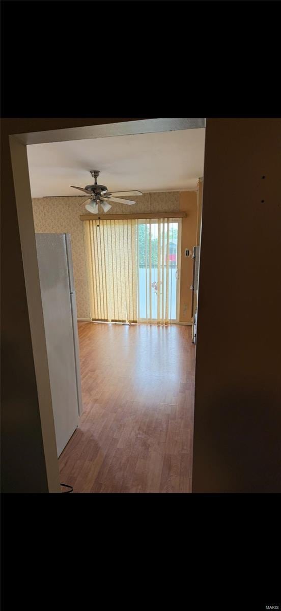 empty room with light wood-style flooring, ceiling fan, and wallpapered walls