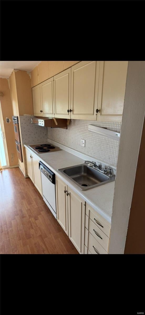 kitchen with light countertops, a sink, multiple ovens, dishwasher, and light wood-style floors