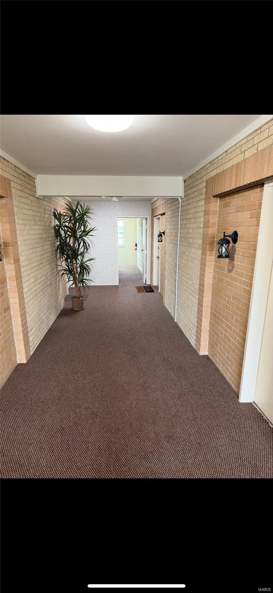 hallway featuring carpet flooring and brick wall