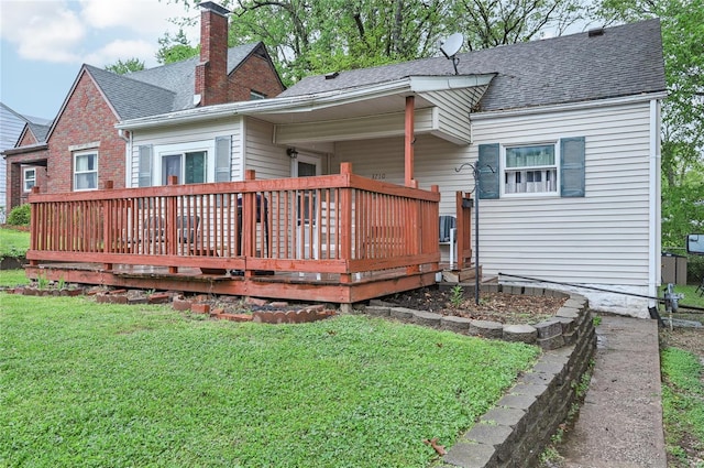 rear view of house featuring a shingled roof, a yard, a deck, and a chimney