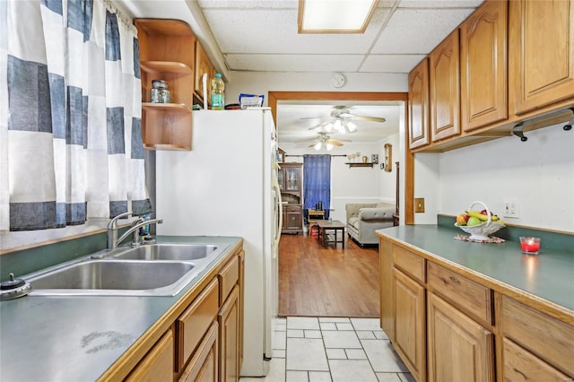 kitchen with a ceiling fan, open shelves, a sink, freestanding refrigerator, and a drop ceiling