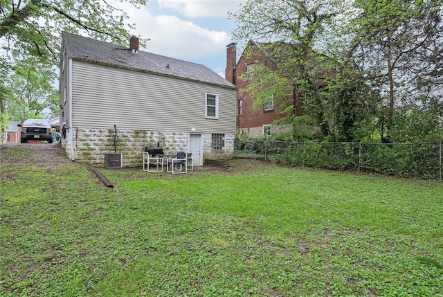 rear view of property with a yard, fence, a chimney, and stone siding