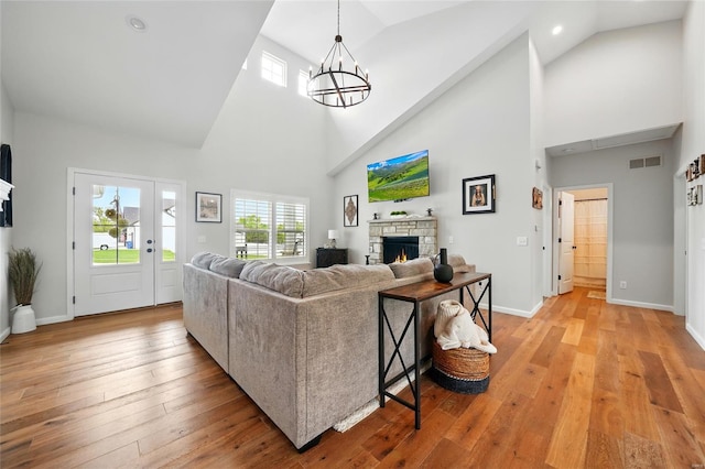living room with visible vents, an inviting chandelier, a fireplace, high vaulted ceiling, and light wood finished floors