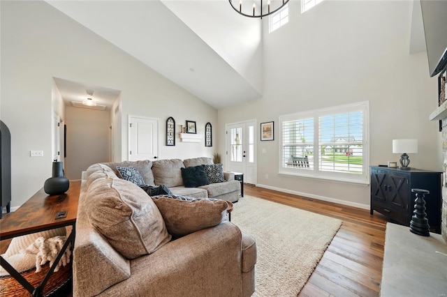 living area featuring attic access, a towering ceiling, wood finished floors, baseboards, and an inviting chandelier